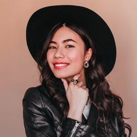 Woman wearing black leather jacket and wide-brimmed hat smiling to the camera.