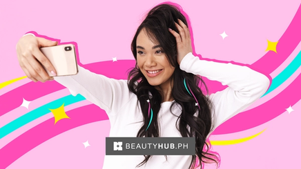 Young, smiling Asian woman touching her hair while taking a selfie