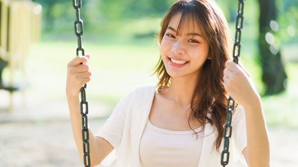 Happy Asian woman with long hair sitting on a swing.