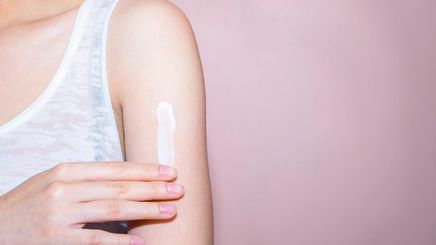 A woman applying lotion to her left arm