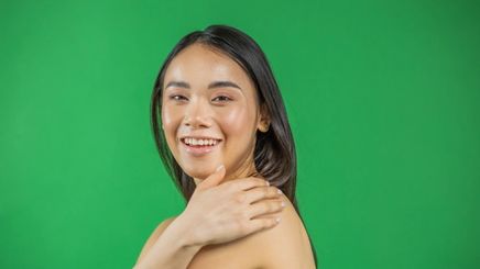 A woman with glowing skin touching her shoulder