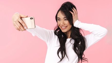 Young, smiling Asian woman touching her hair while taking a selfie