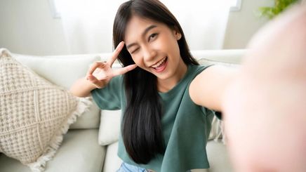 Smiling Asian woman with peace fingers sign and taking a selfie