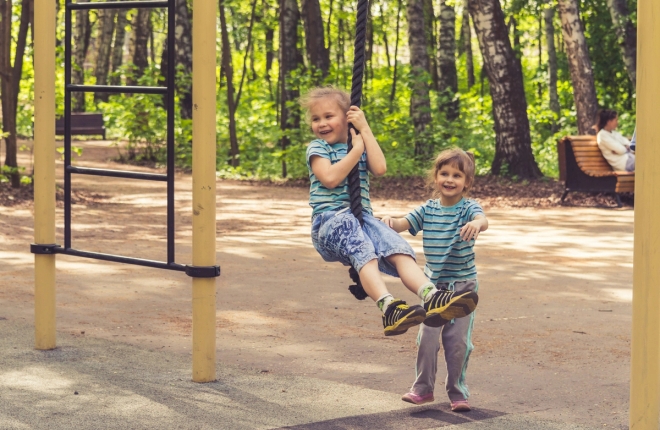 To jenter leker på huske i skolegård.