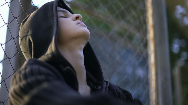 Lei tenåring med hettegenser lener hodet bakover og lukker øynene.