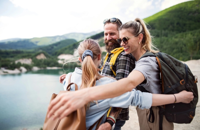 Smilende foreldre klemmer tenåringsdatter på tur i flott natur.