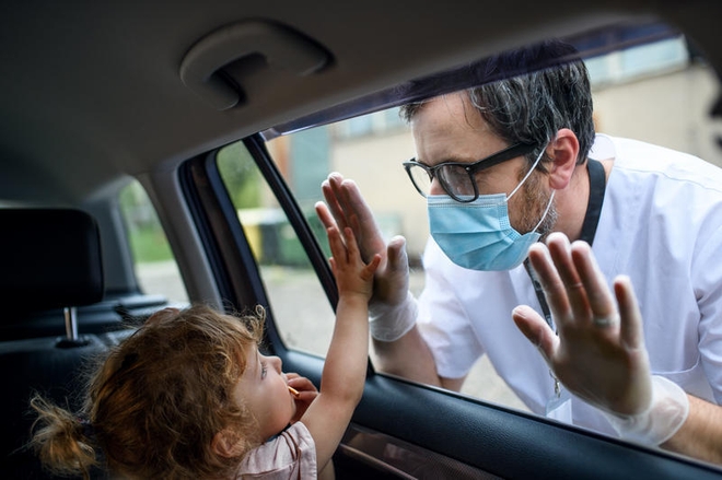 Mannlig sykepleier iført munnbind snakker med jente som sitter inne i en bil.