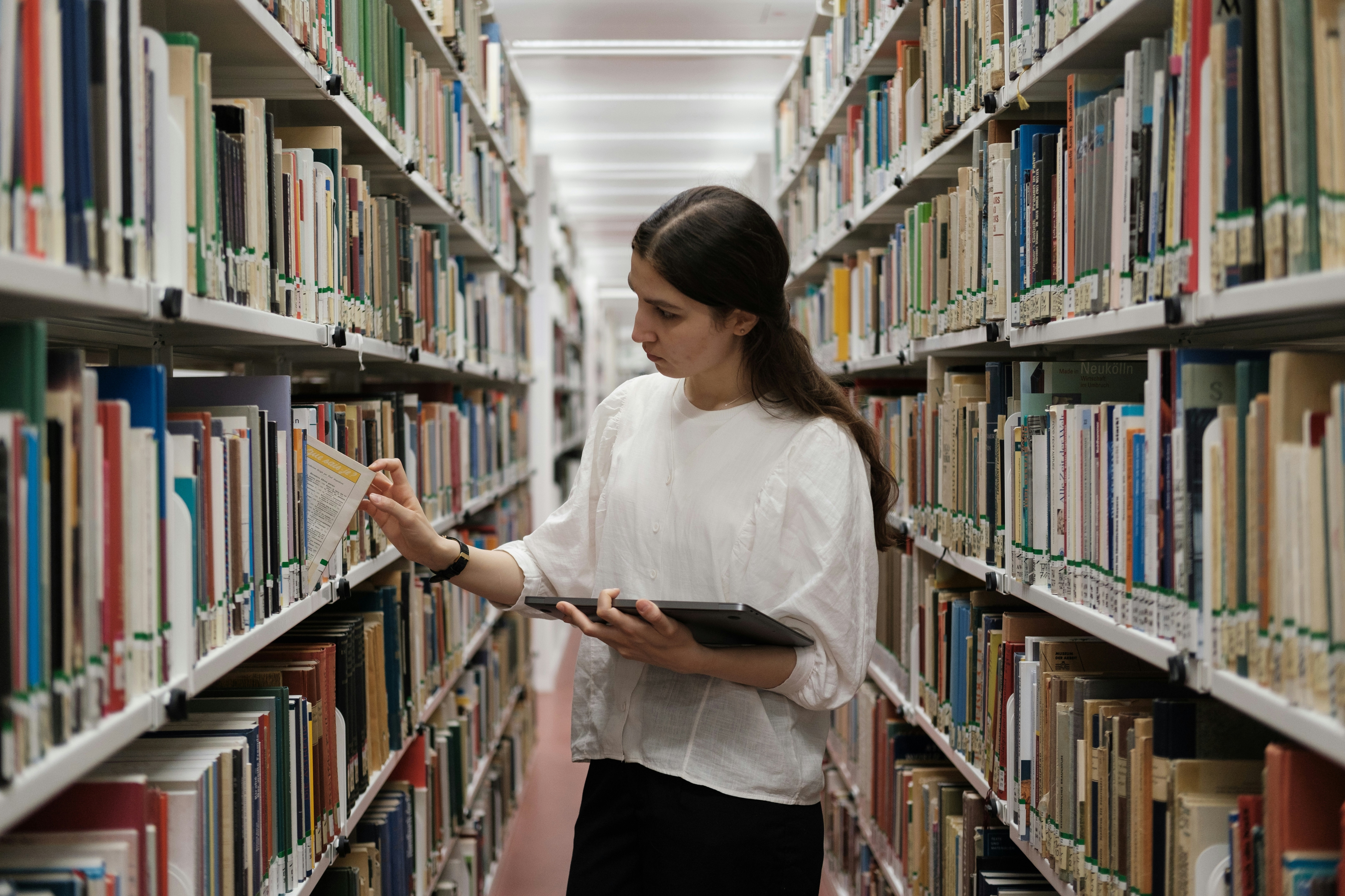 Kvinne tar ut bok fra bibliotekshylle.