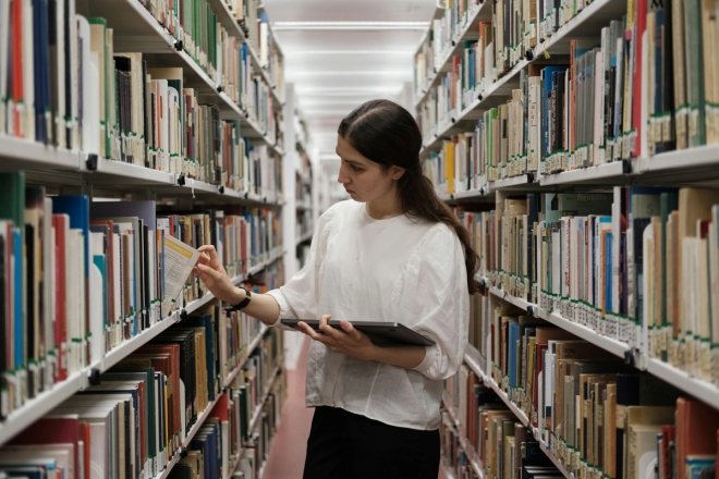 Kvinne tar ut bok fra bibliotekshylle.
