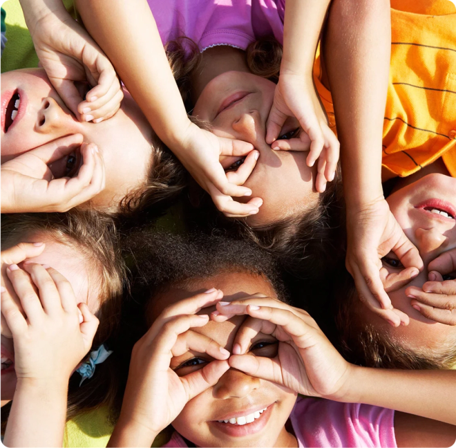 Barn ligger på bakken i sirkel og holder hendene foran ansiktet i "brilleformasjon".