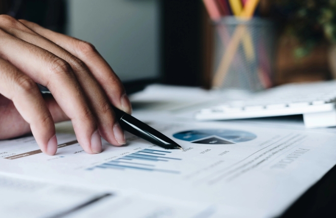 Hånd holder penn over papir med grafer.