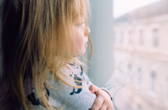 Liten trist jente ser ut av vinduet.