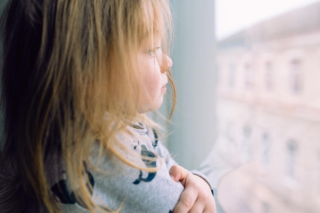 Liten trist jente ser ut av vinduet.