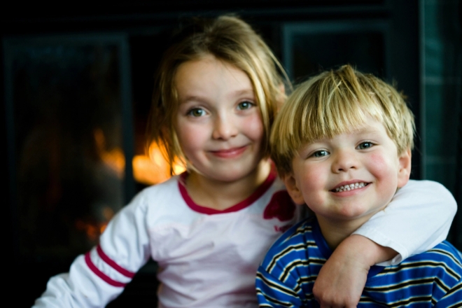 Storesøster holder armen rundt lillebror. De smiler mot kameraet.