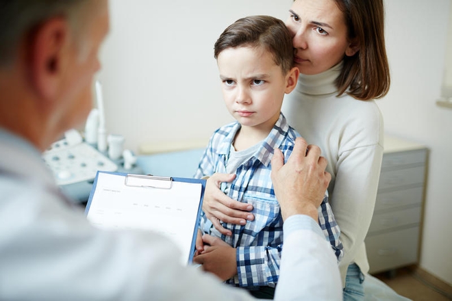 Skeptisk gutt på legekontor, sittende på mammas fang.