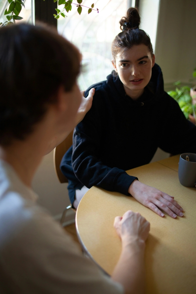 Forelder og tenåringsjente i samtale sittende ved et kjøkkenbord.