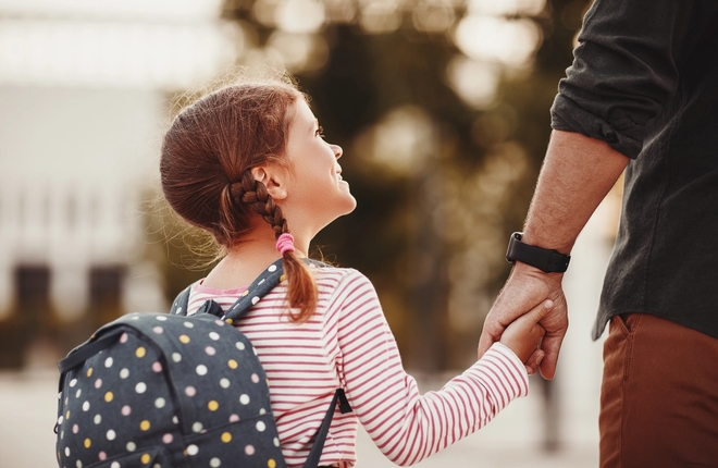Far holder datters hånd på vei til første skoledag. Foto: Adobe Stock