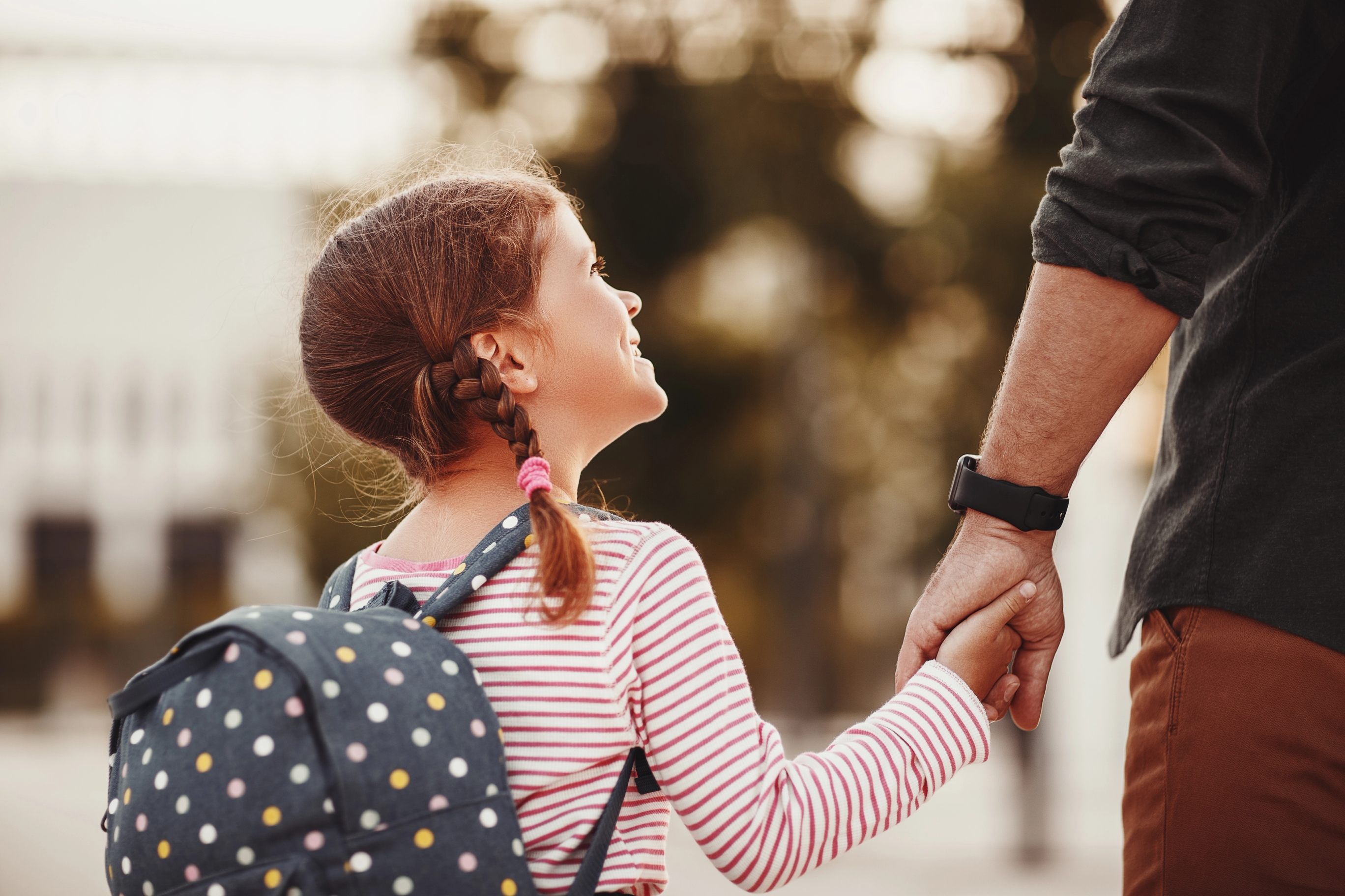 Far holder datters hånd på vei til første skoledag. Foto: Adobe Stock