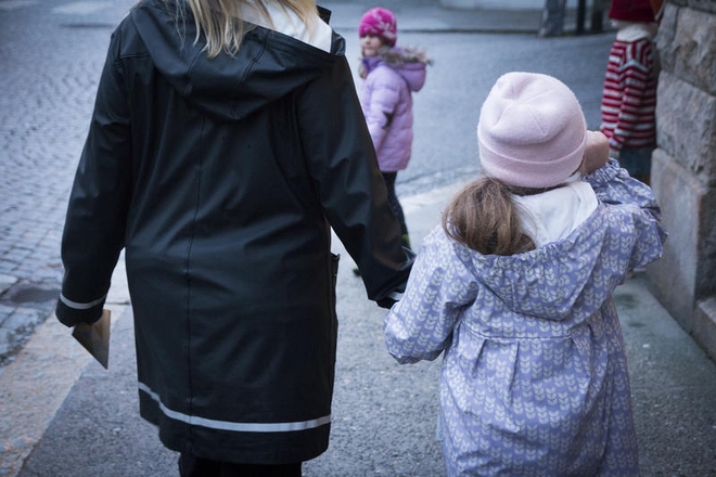 Voksen kvinne leier en jente i hånda. De er fotografert utendørs, bakfra.