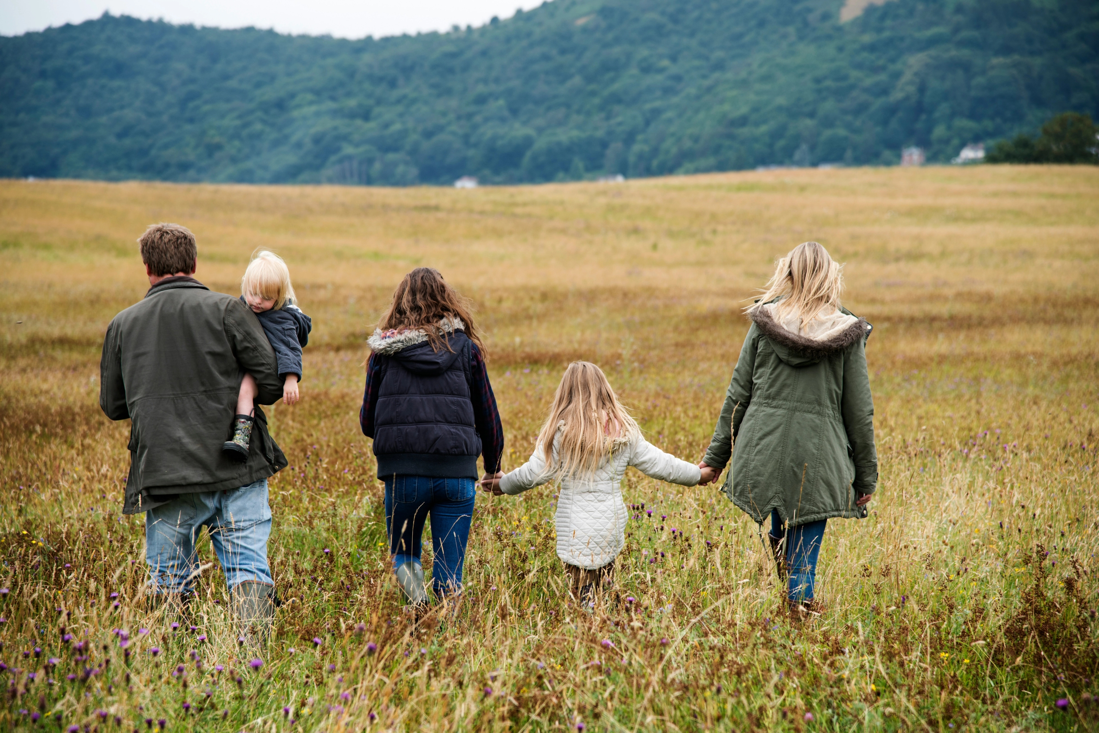 Familie går tur over gresslette med ryggene vendt mot kamera.