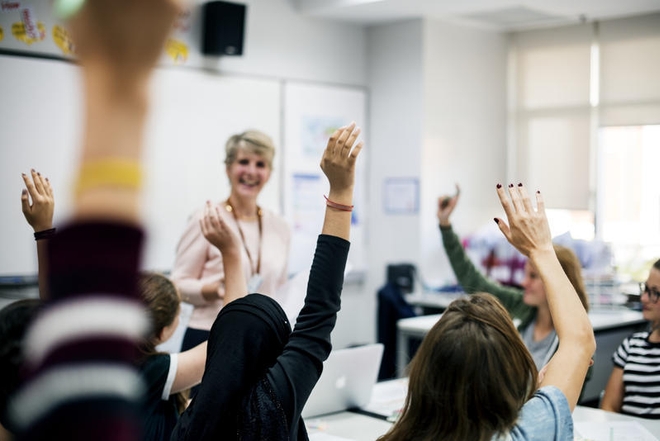 Lærer i klasserom med elever som rekker opp hendene.