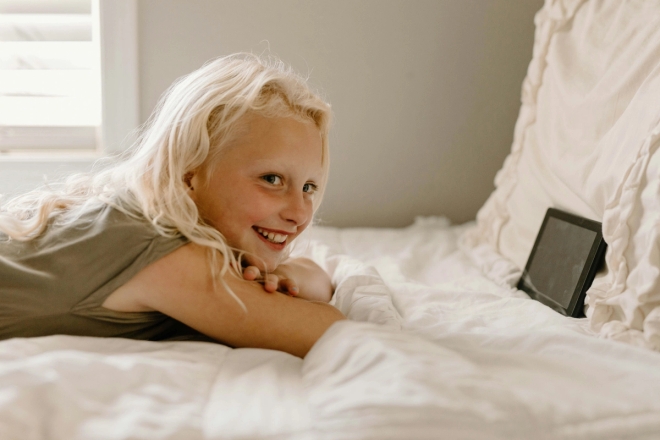 Jente ser på tablet smilende liggende på senga.