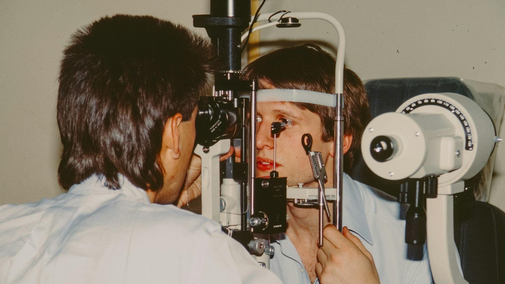 Optométriste examinant l'œil d'un patient avec un instrument, illustration du suivi ophtalmologique après un décollement de la rétine