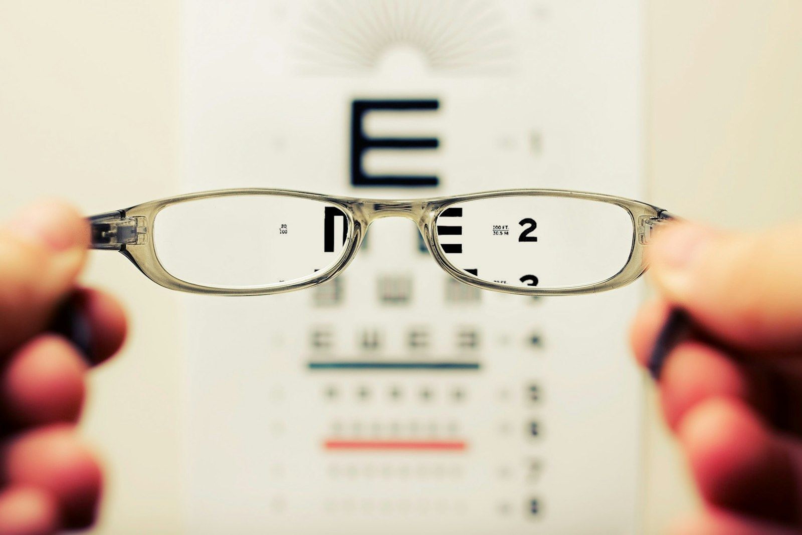 Mains tenant une paire de lunettes devant un tableau de test de vue, illustrant la remise d'équipement à un client le jour J