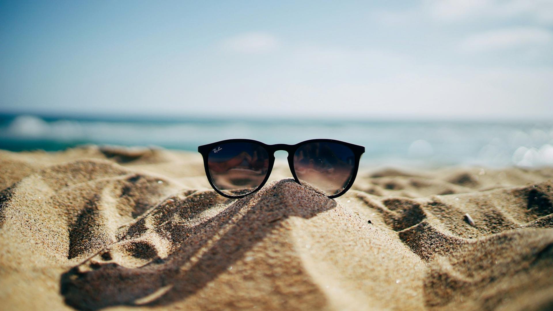 Lunettes de soleil à monture noire posées sur le sable face à la mer, illustrant la protection contre l'éblouissement