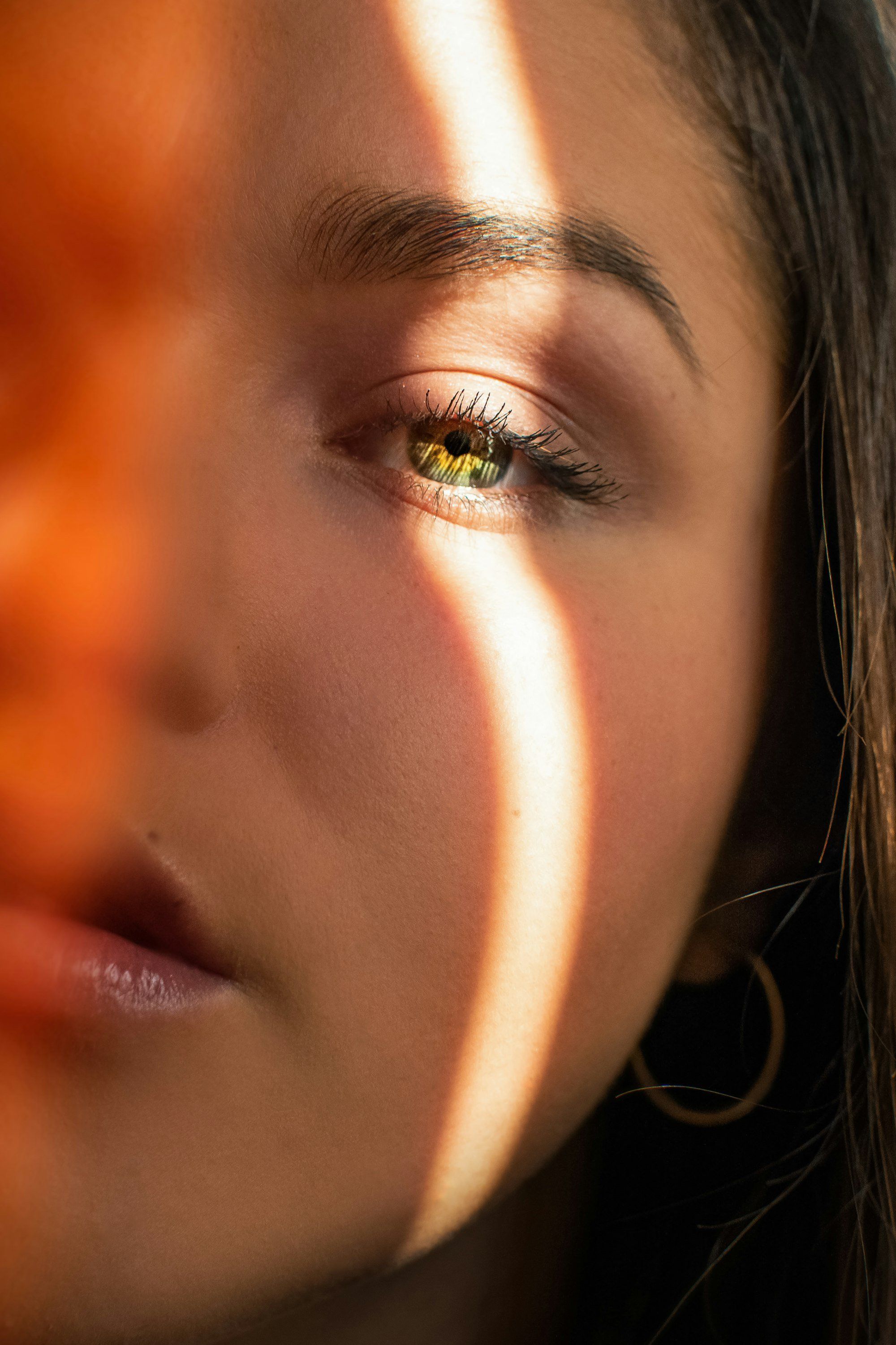 Portrait d'une femme dont le visage est éclairé par une lumière vive traversant des stores, illustrant l'inconfort oculaire face à la lumière