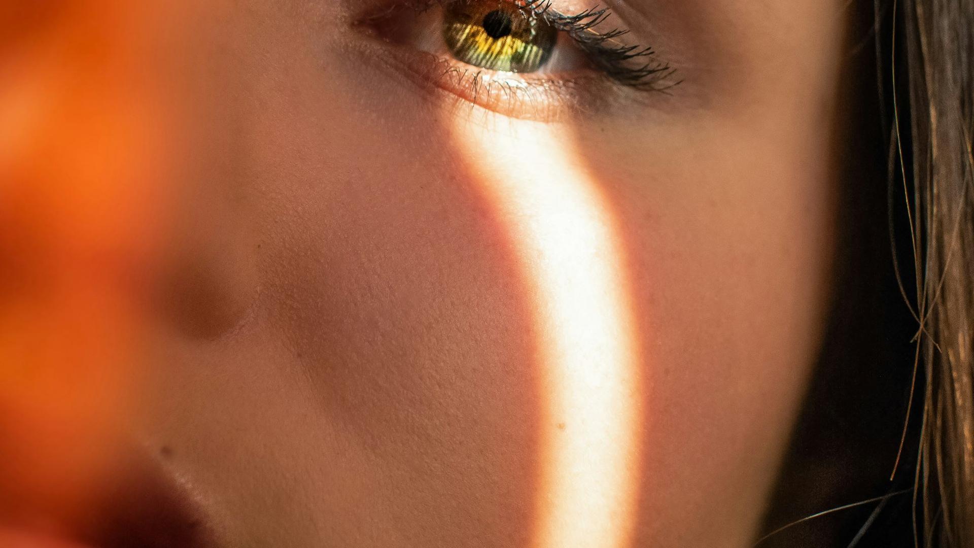 Portrait d'une femme dont le visage est éclairé par une lumière vive traversant des stores, illustrant l'inconfort oculaire face à la lumière