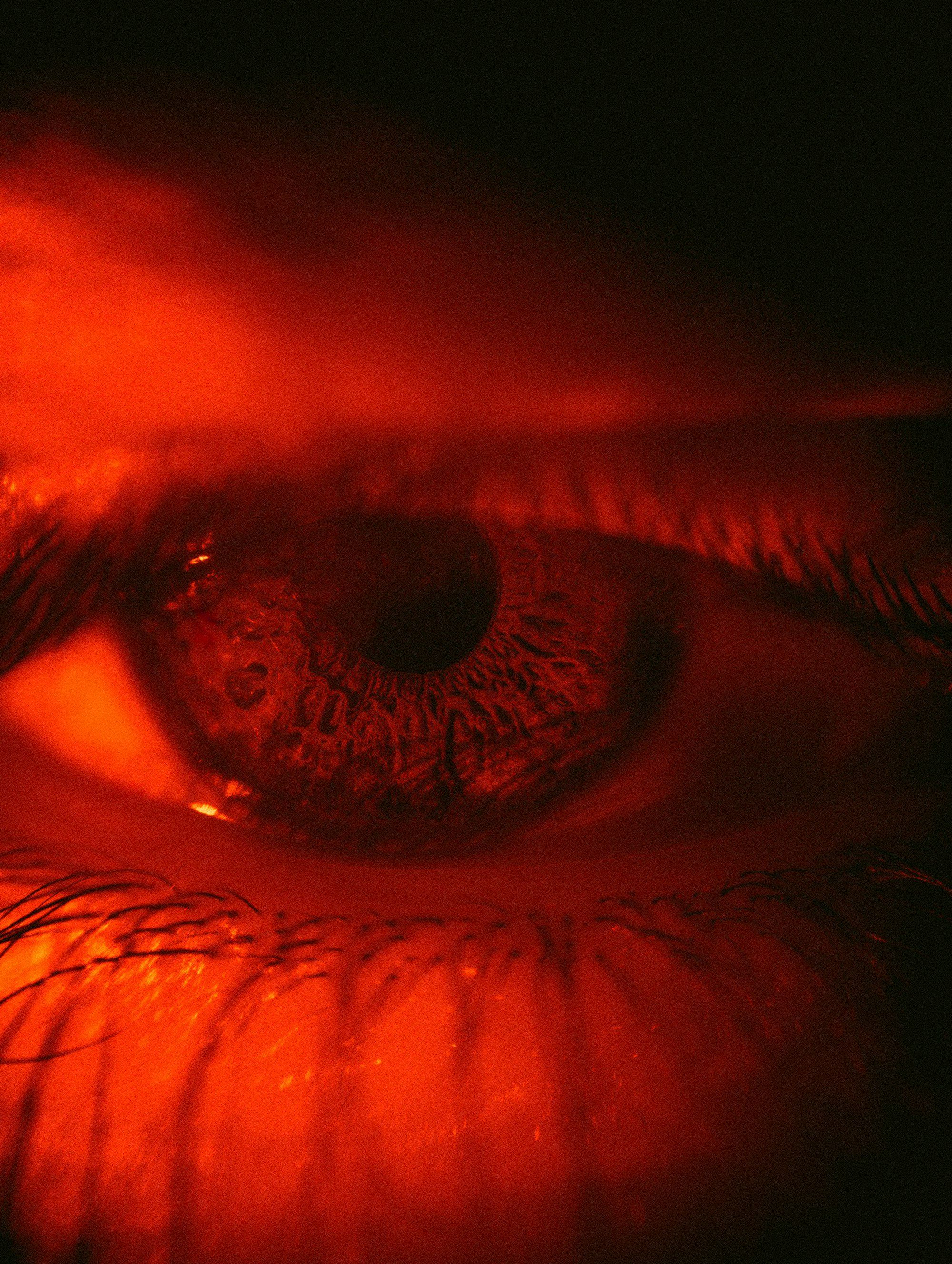 Gros plan sur un œil humain éclairé d'une lumière rouge, illustration de la rougeur oculaire