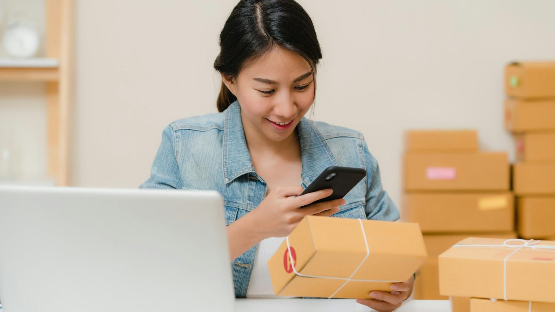 Professionnelle vérifiant une commande en ligne entre ordinateur et cartons, gestion d'une boutique e-commerce