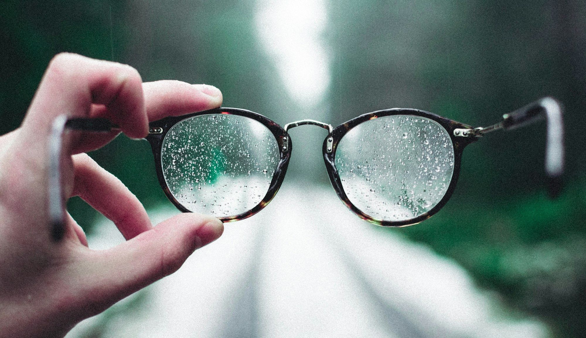 Mains tenant une paire de lunettes avec des gouttelettes d'eau, illustrant la manipulation et le contrôle des verres dans l'atelier de l'opticien.