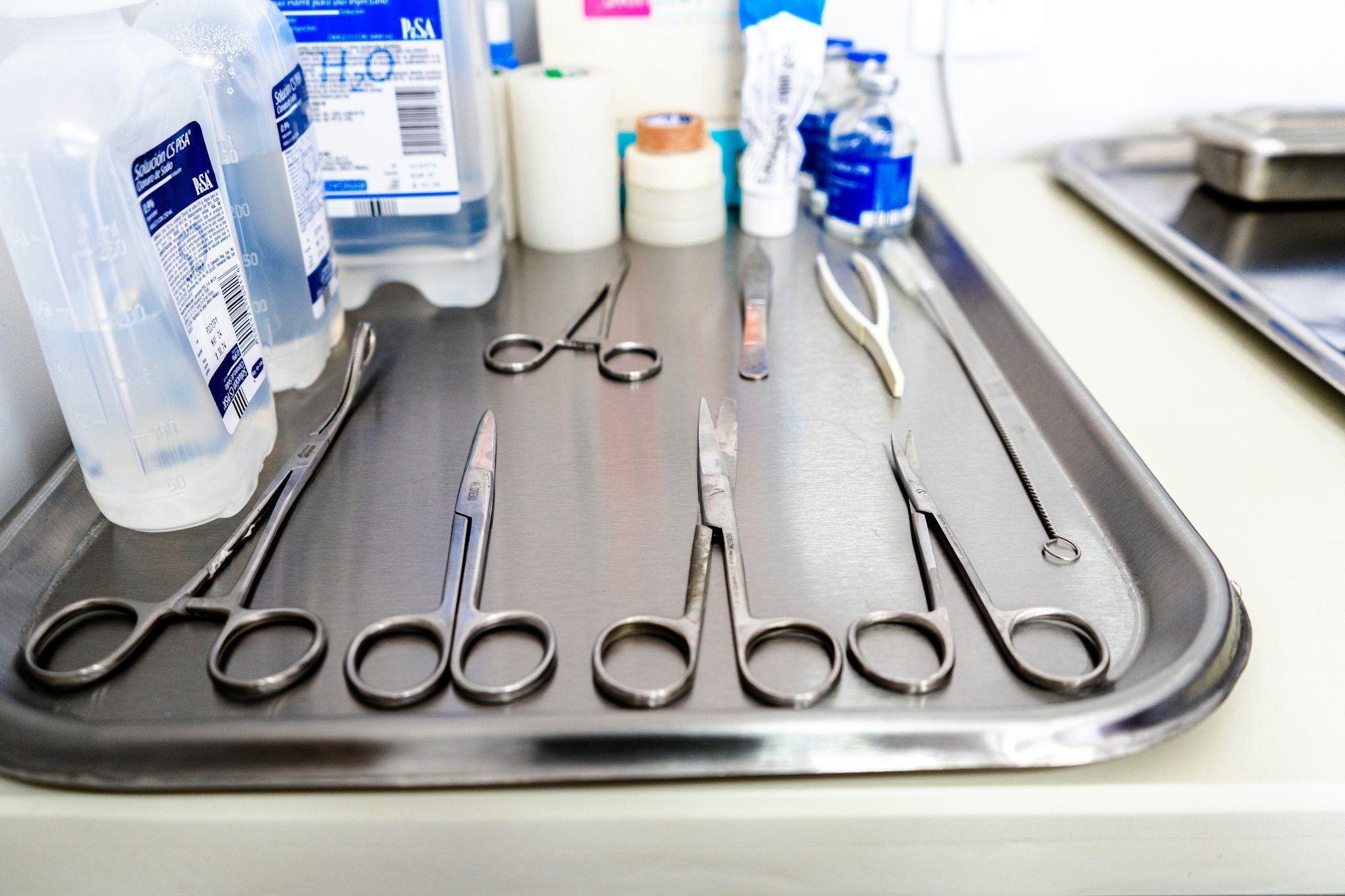 Plateau métallique contenant ciseaux et instruments de précision, illustrant le petit outillage d'un atelier d'optique.