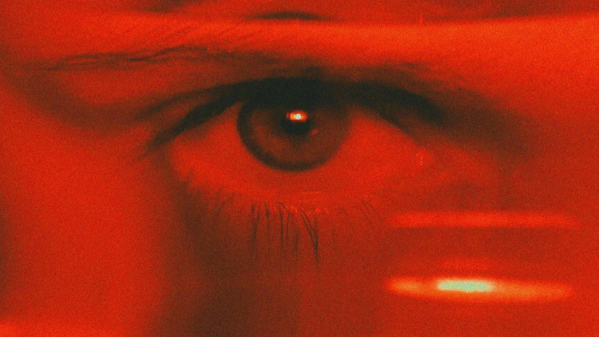 Gros plan sur un œil humain éclairé d'une lumière rouge, évoquant l'irritation et la douleur ressenties lors d'une kératite