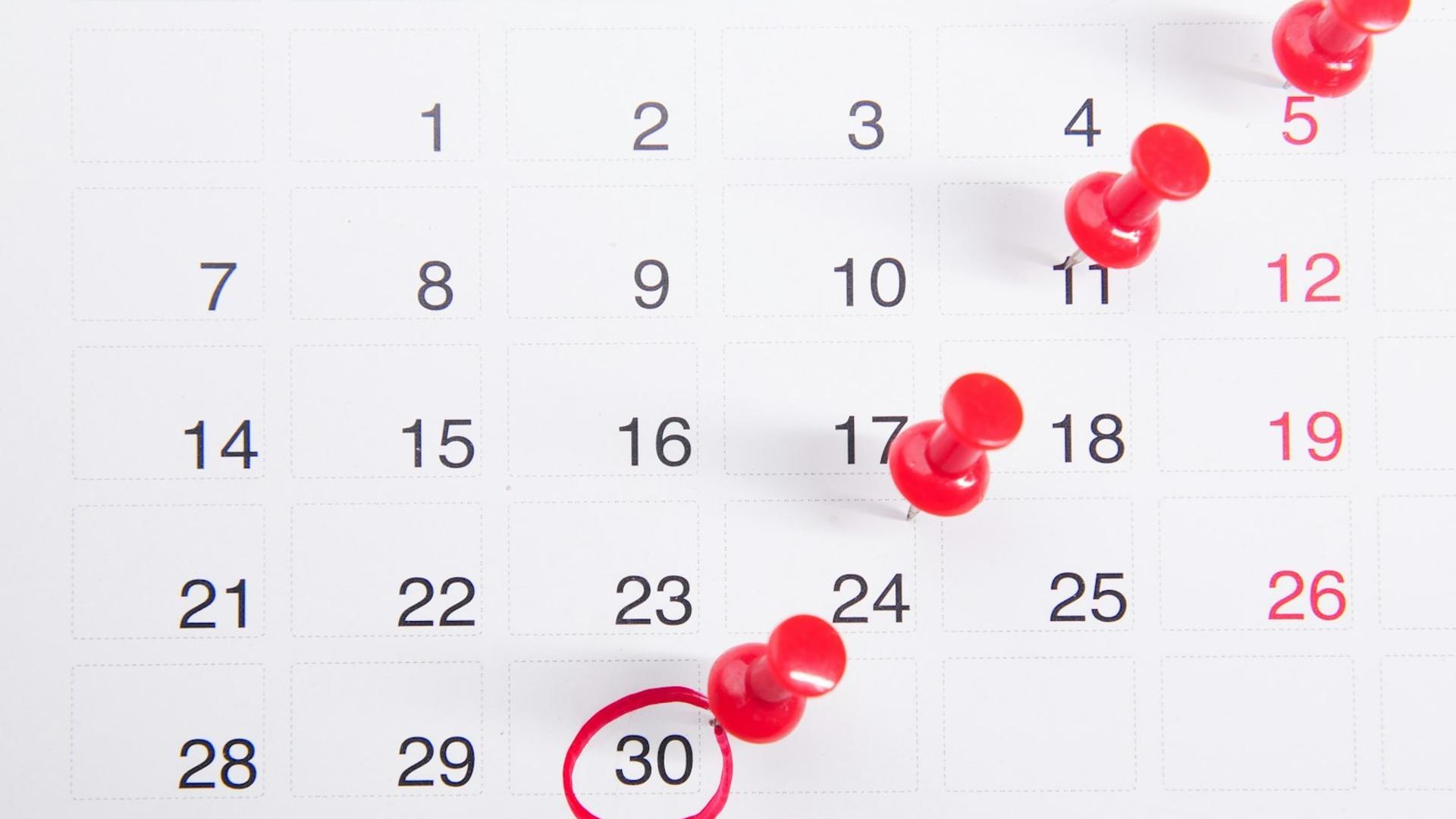 Calendrier mural avec des punaises rouges sur des dates clés, symbolisant la planification des rendez-vous et de l'équipe avant un pic