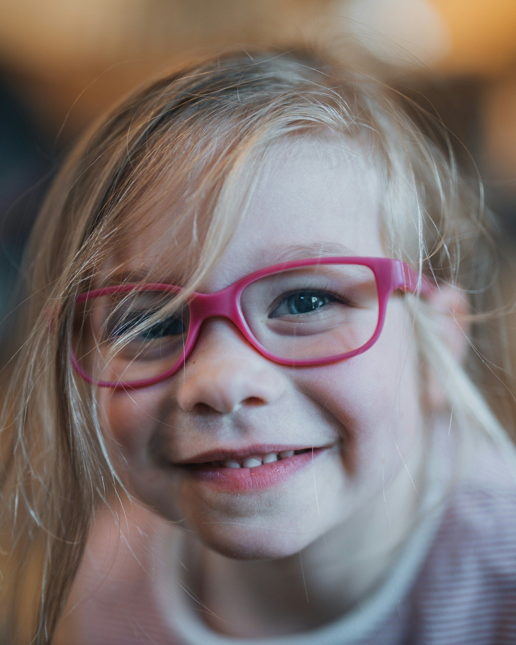 Petite fille souriante portant des lunettes roses, le port de lunettes étant le premier traitement de l'amblyopie chez l'enfant