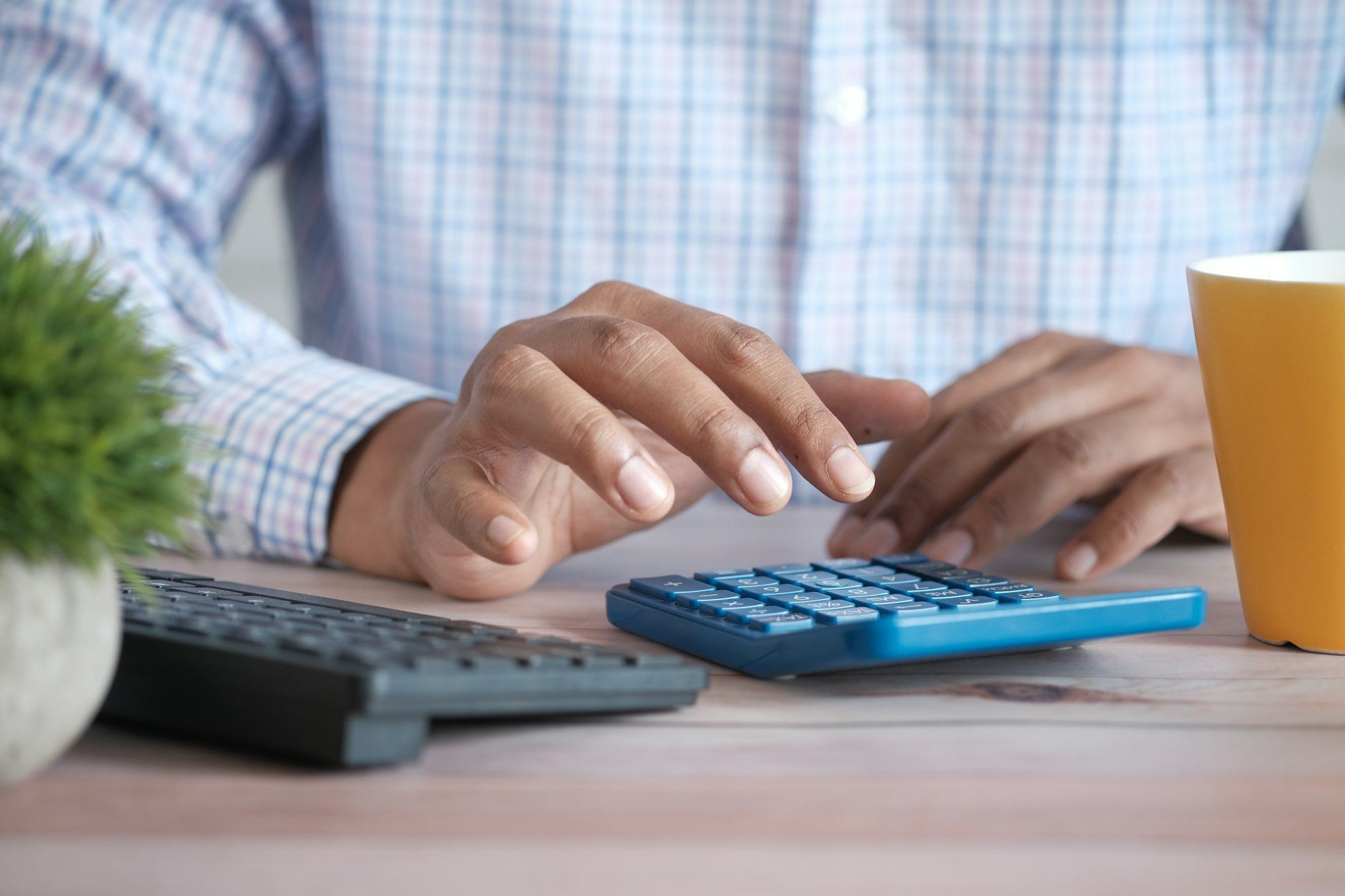 Main qui utilise une calculatrice sur un bureau, calcul du plan de financement d'un projet d'opticien