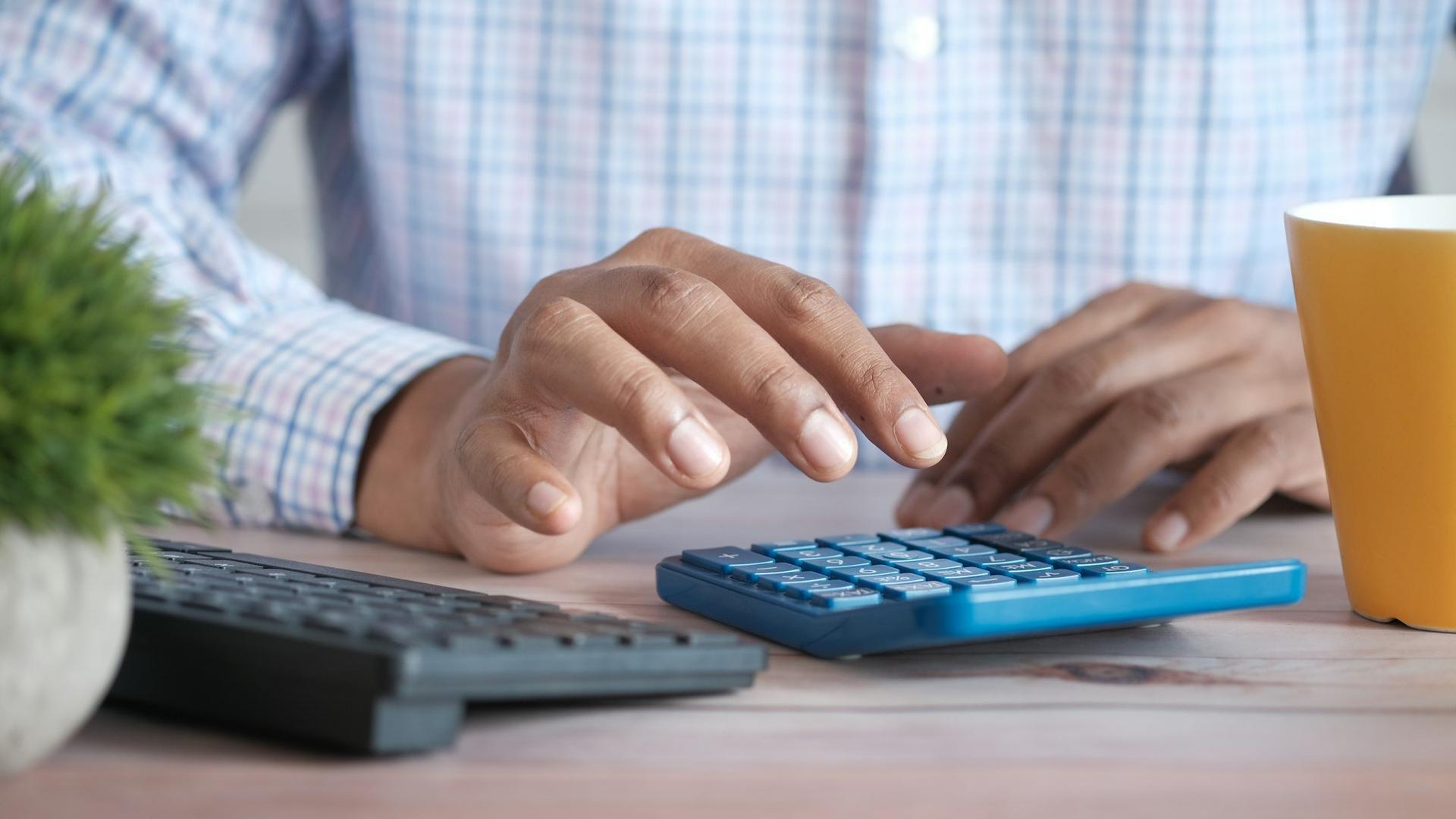 Main qui utilise une calculatrice sur un bureau, calcul du plan de financement d'un projet d'opticien