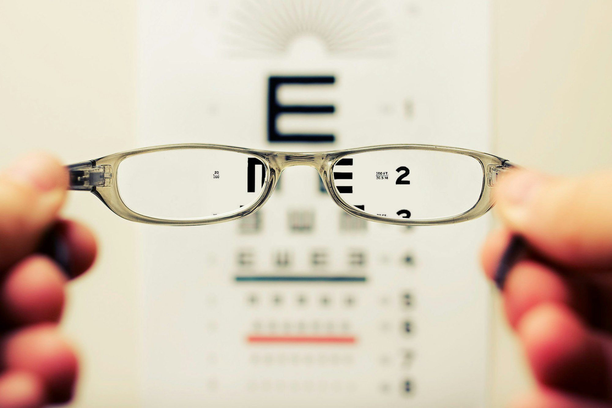 Lunettes tenues devant un tableau de test de vue, la correction optique restant utile pour préserver l'œil sain chez l'adulte amblyope