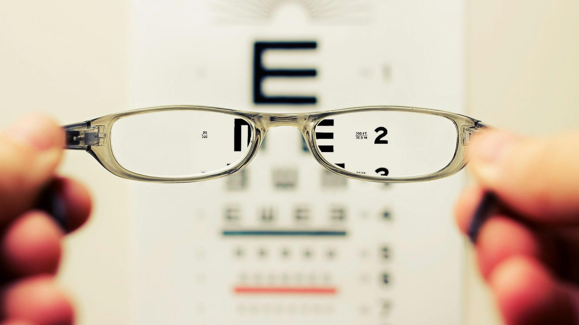 Lunettes tenues devant un tableau de test de vue, la correction optique restant utile pour préserver l'œil sain chez l'adulte amblyope