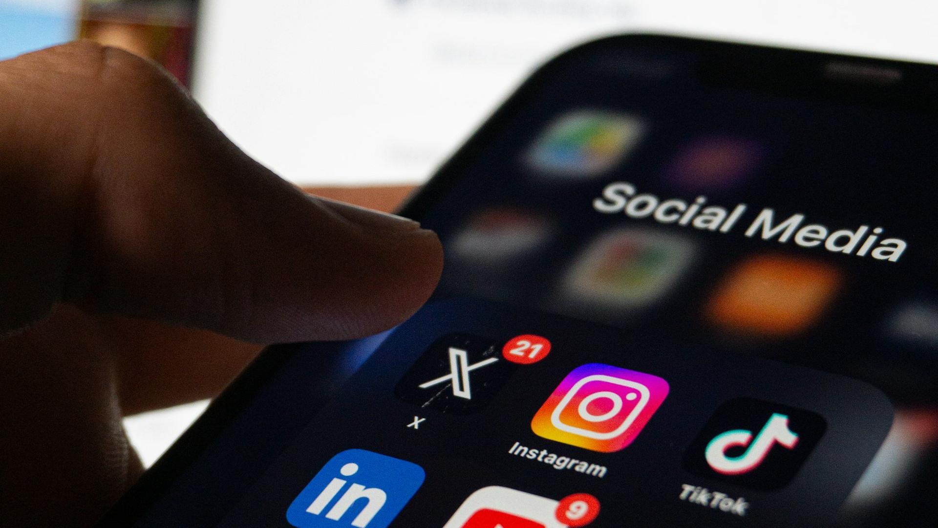 Opticienne tenant son smartphone avec les applications de réseaux sociaux visibles à l'écran, pour illustrer la présence en ligne d'une boutique d'optique