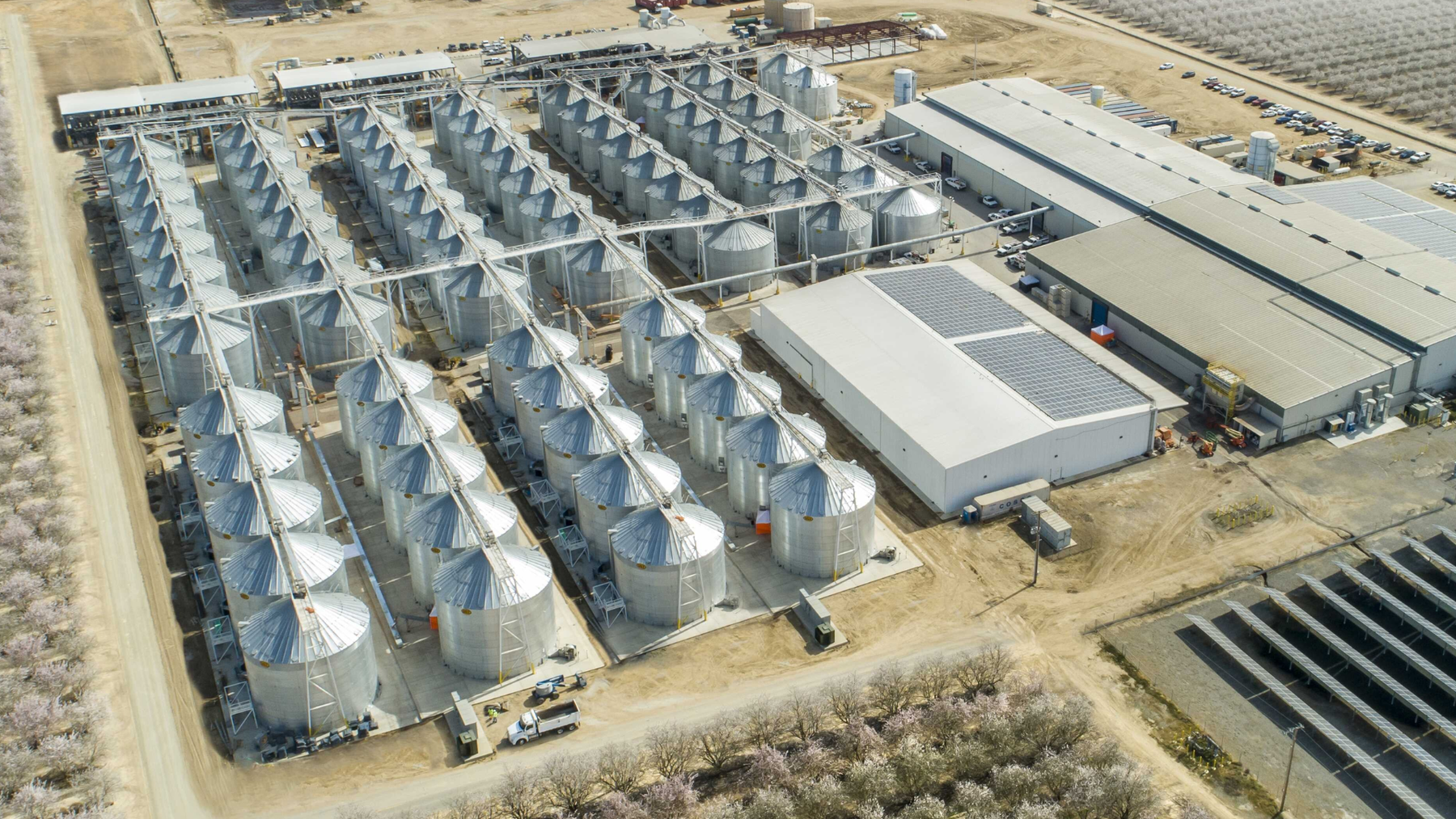 Aerial view of the Primex Farms pistachio processing plant in Wasco, California, with rows of steel silos beside a warehouse and orchards