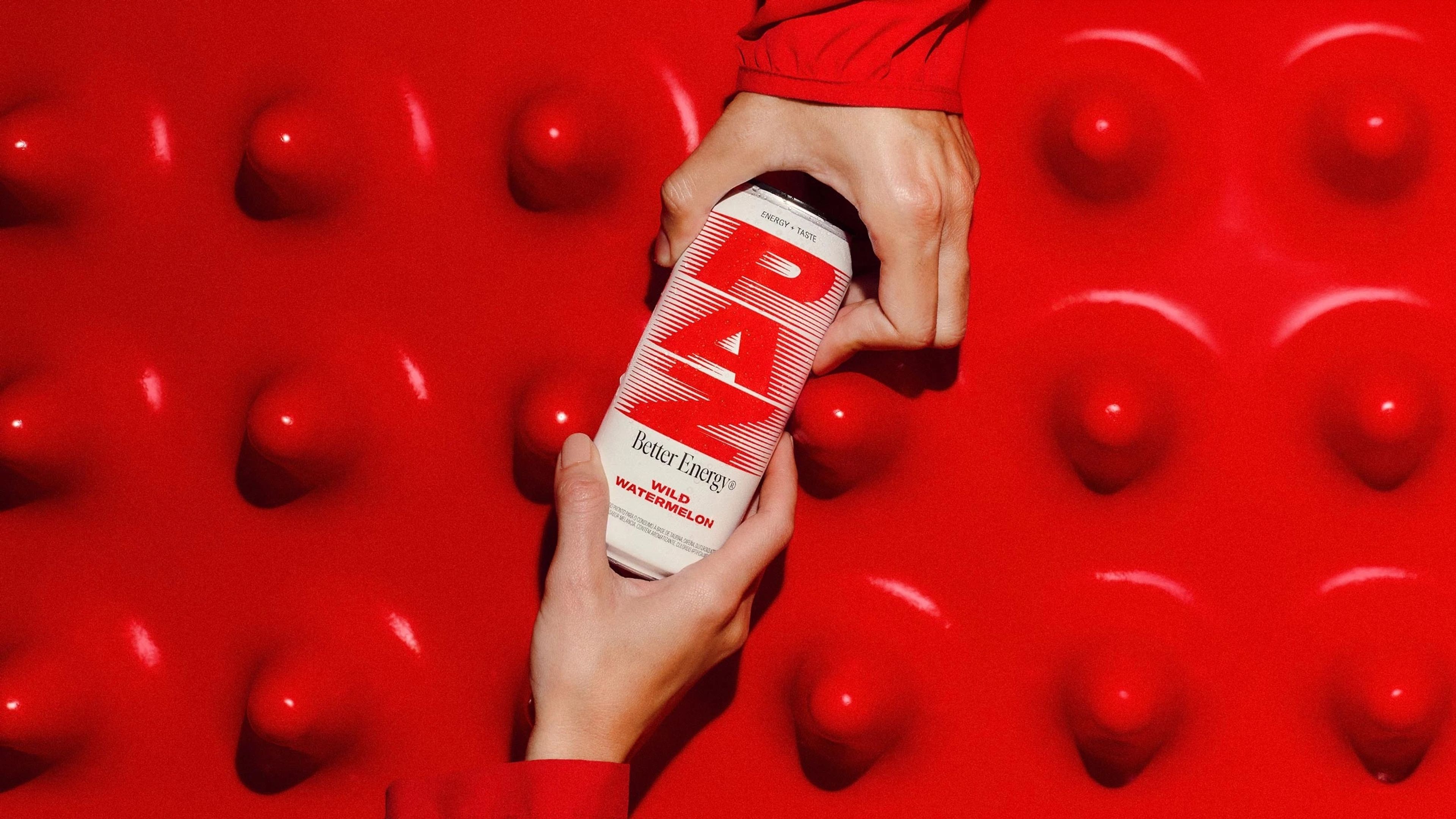 Paz energy drink can held against a red bumpy surface.
