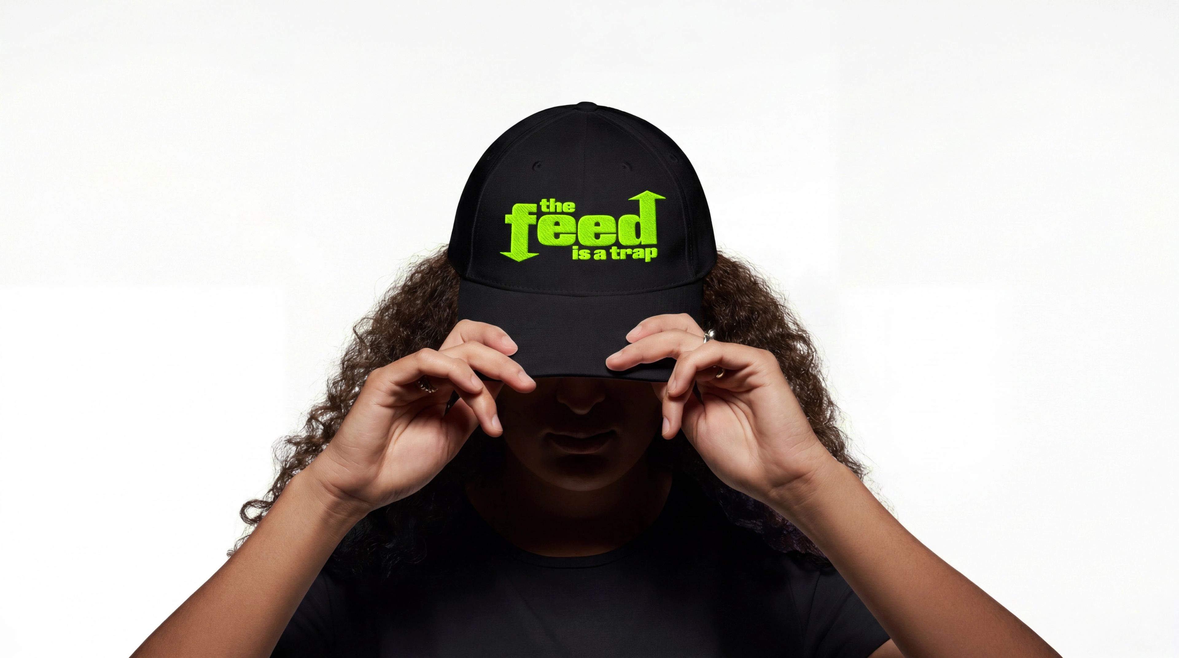 Man pulling down a black cap with a green "the feed is a trip" logo.