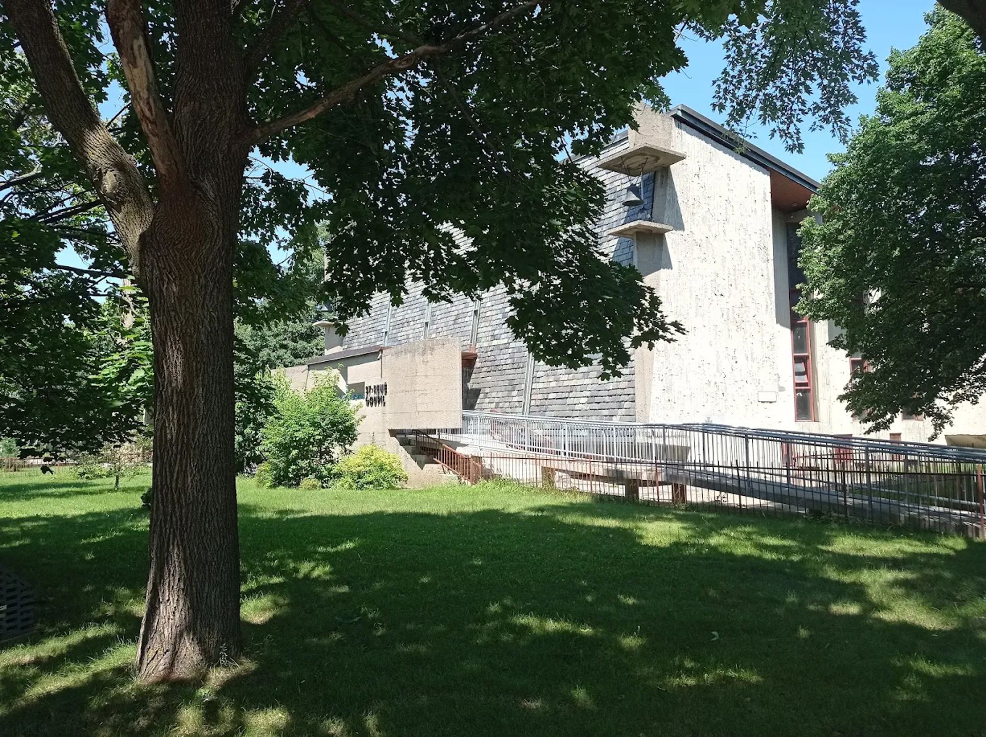 Vue extérieure de l’église, de la pelouse et d’une longue allée bordée de garde-corps