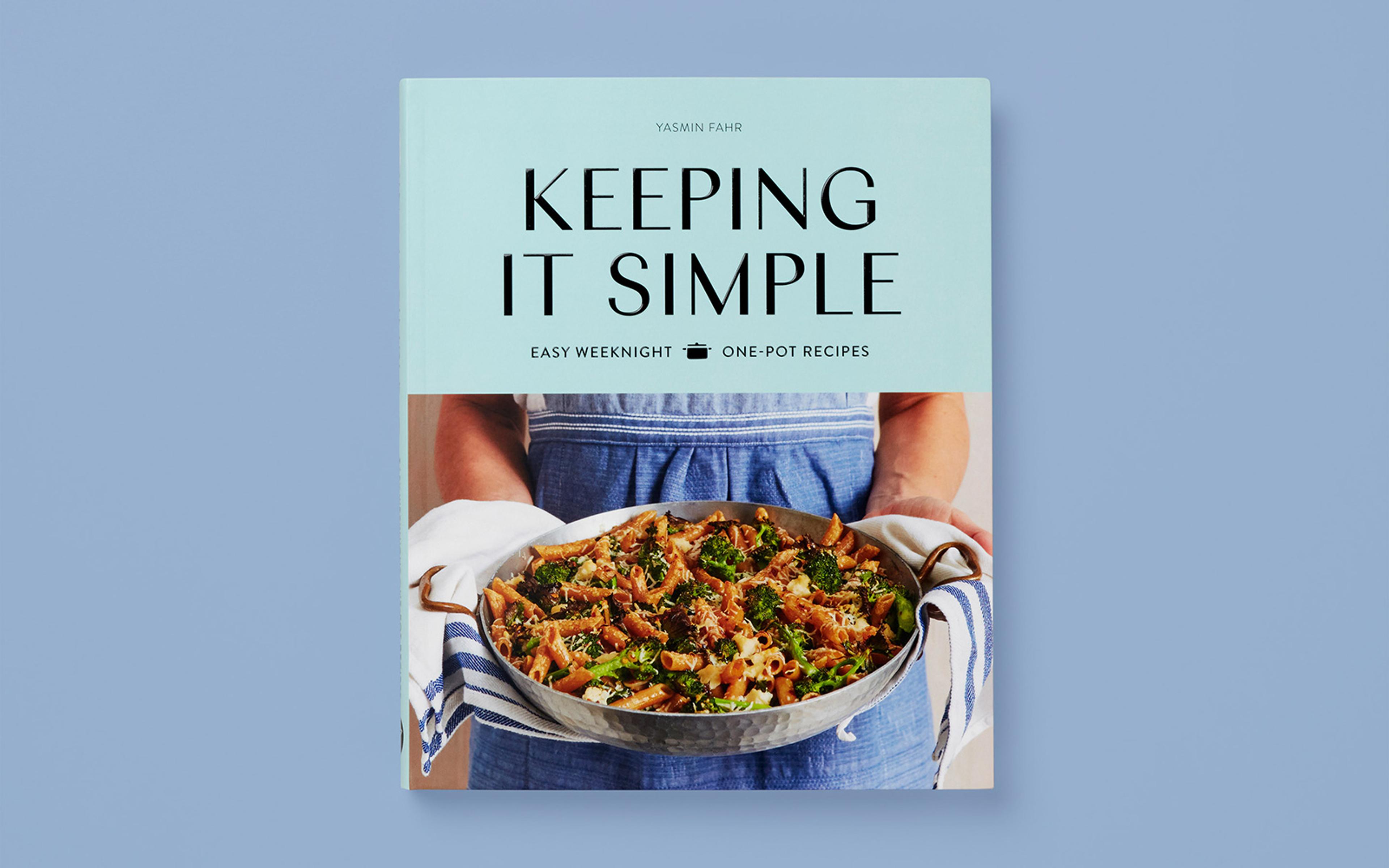 Pale blue book cover titled "Keeping It Simple" by Yasmin Fahr, featuring a photograph of a person holding a pan of pasta and vegetables, with the subtitle "Easy weeknight one-pot recipes," set against a light grey background.