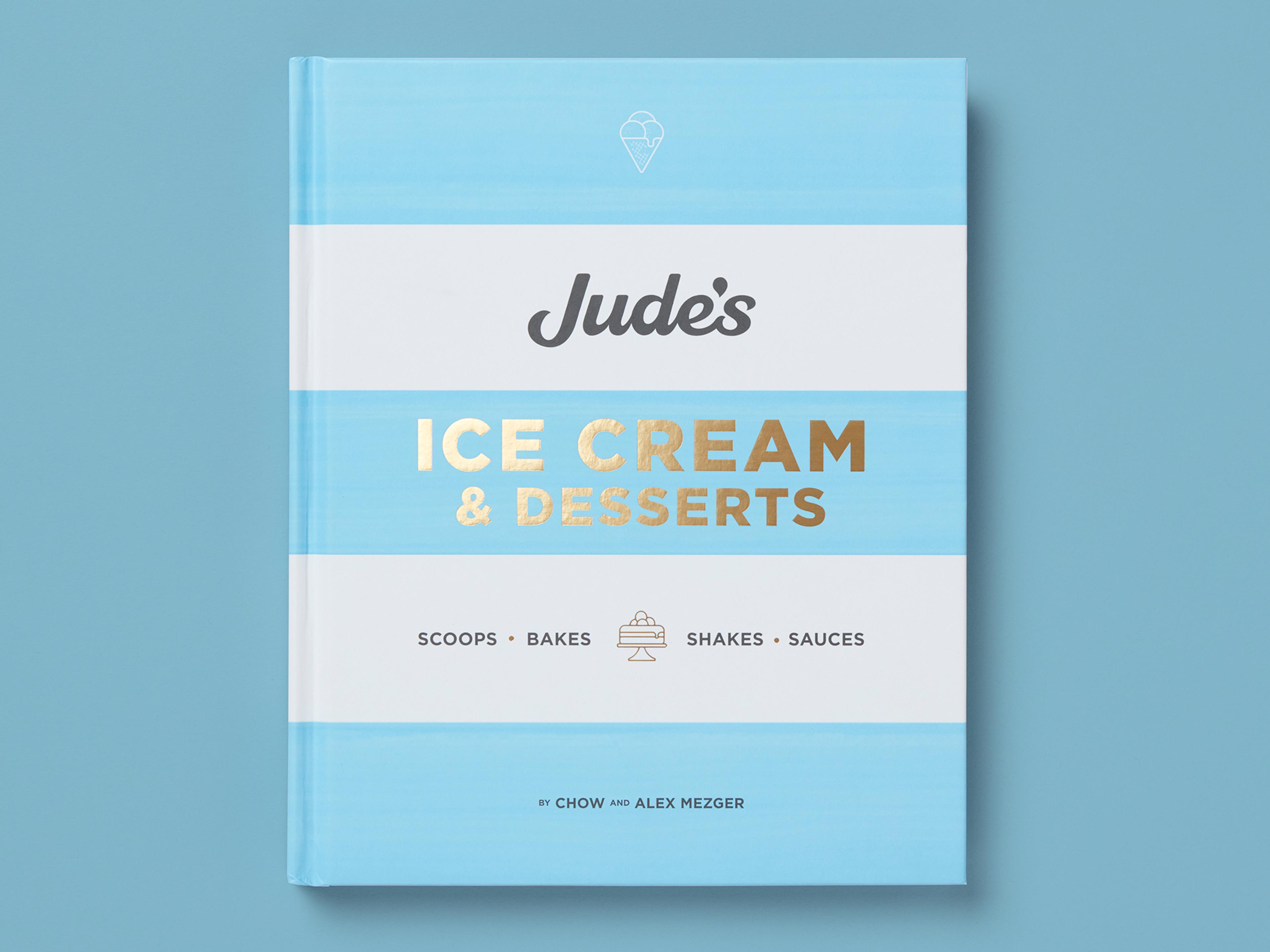 Book titled "Jude’s Ice Cream & Desserts" on a pale blue background, with soft horizontal stripes and gold-foil lettering. Subheading lists "Scoops, Bakes, Shakes, Sauces," with a small dessert icon and author credit to Chow and Alex Mezger at the bottom.