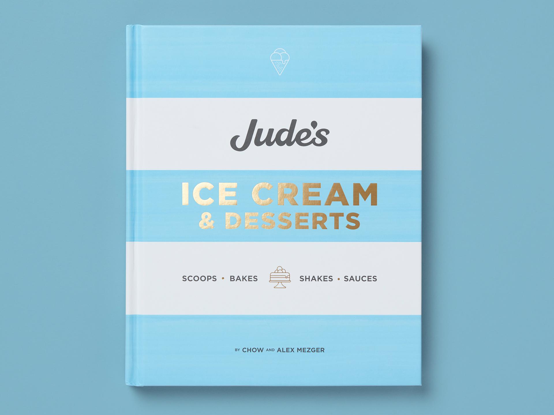 Book titled "Jude’s Ice Cream & Desserts" on a pale blue background, with soft horizontal stripes and gold-foil lettering. Subheading lists "Scoops, Bakes, Shakes, Sauces," with a small dessert icon and author credit to Chow and Alex Mezger at the bottom.